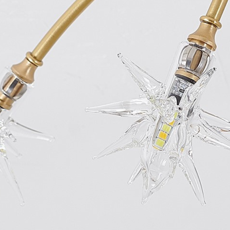 Close view of a clear moulded glass star diffuser and G4 LED bulb on a gold arm of the Nevaro ceiling light