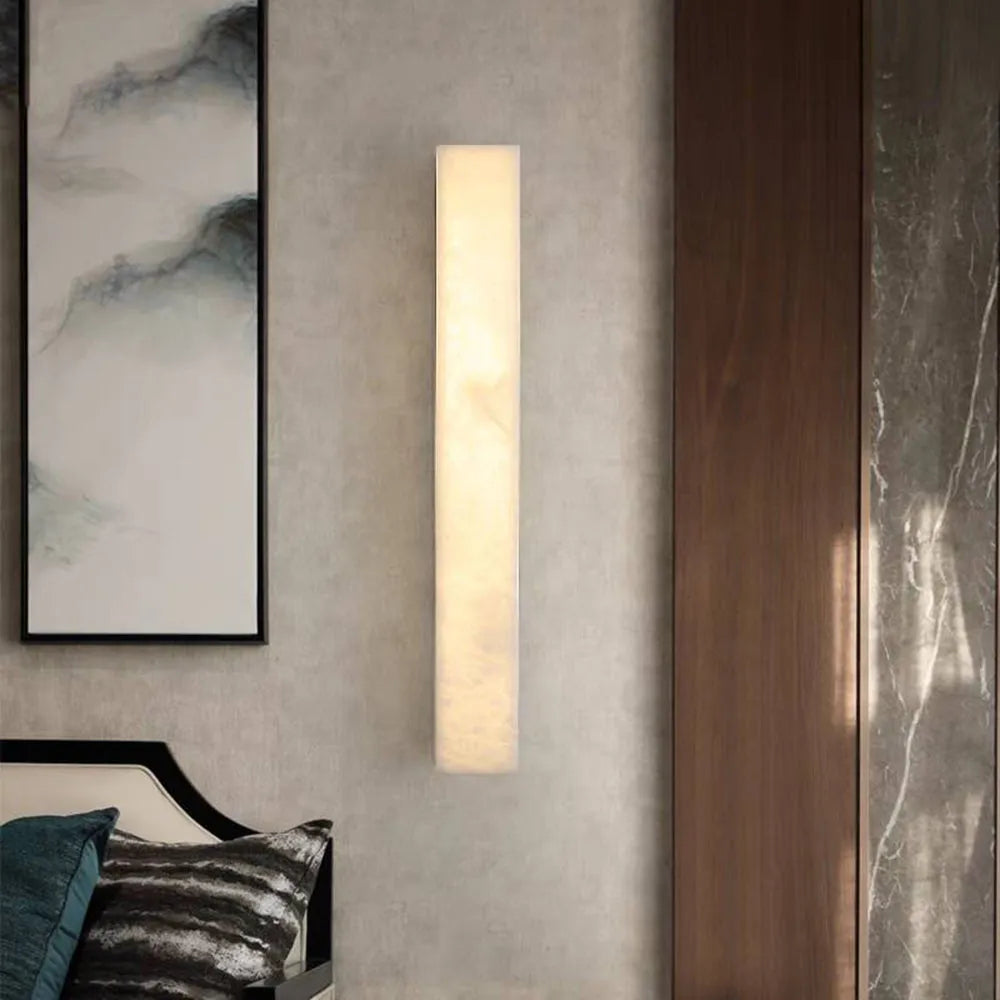 Ayro wall light mounted on a plaster wall next to a dark timber panel, casting an even vertical wash of warm light