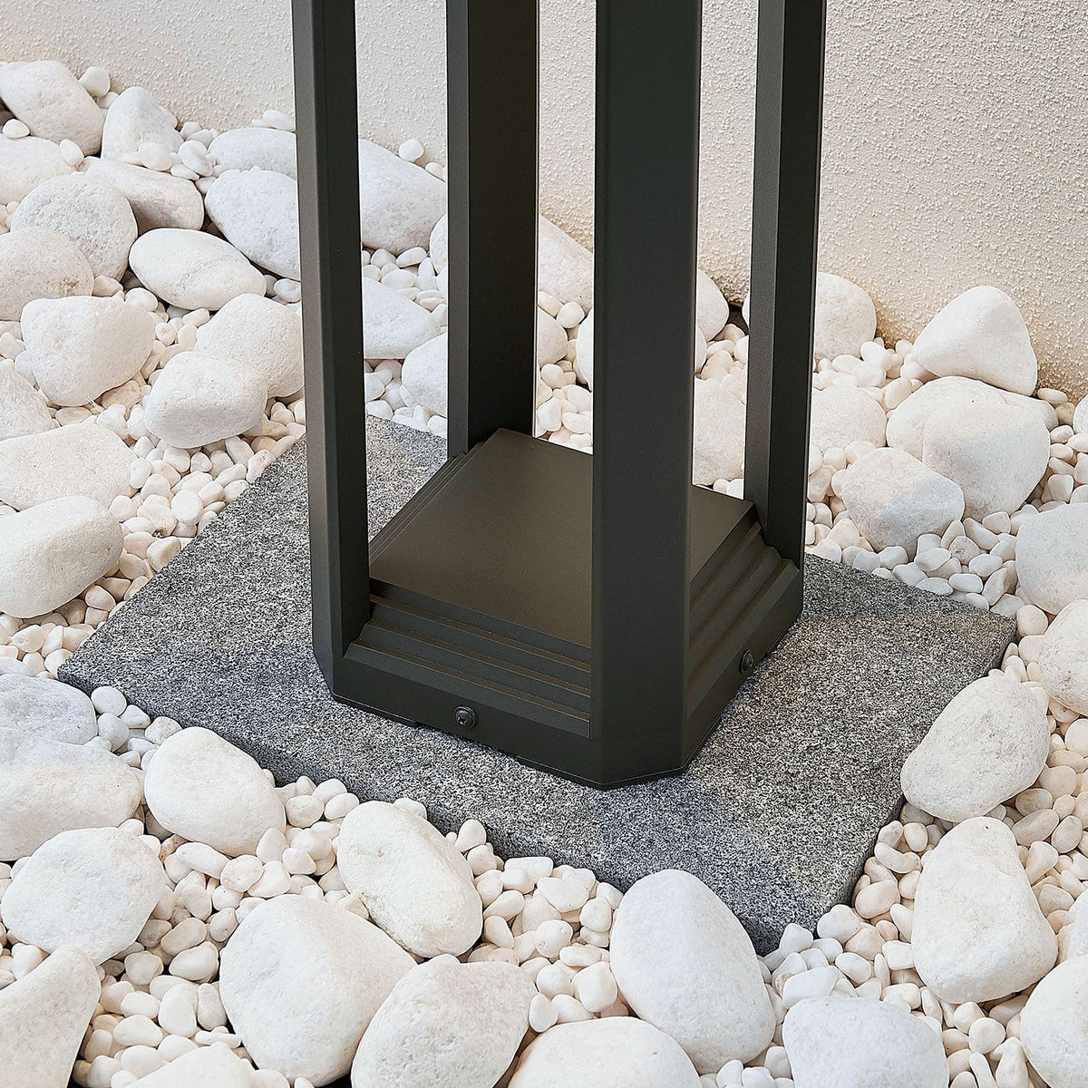 Base of the Feryn path light fixed to a paving slab among white garden pebbles