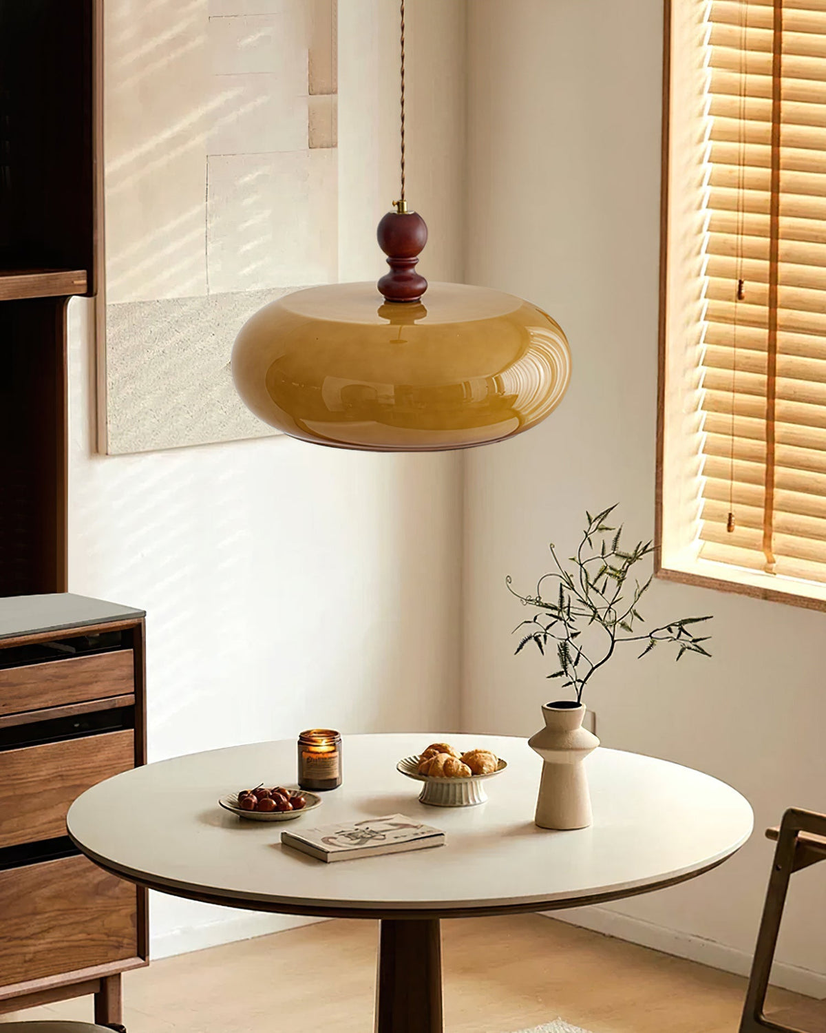 Halvo amber glass pendant light above a round dining table in a sunlit room with wooden blinds