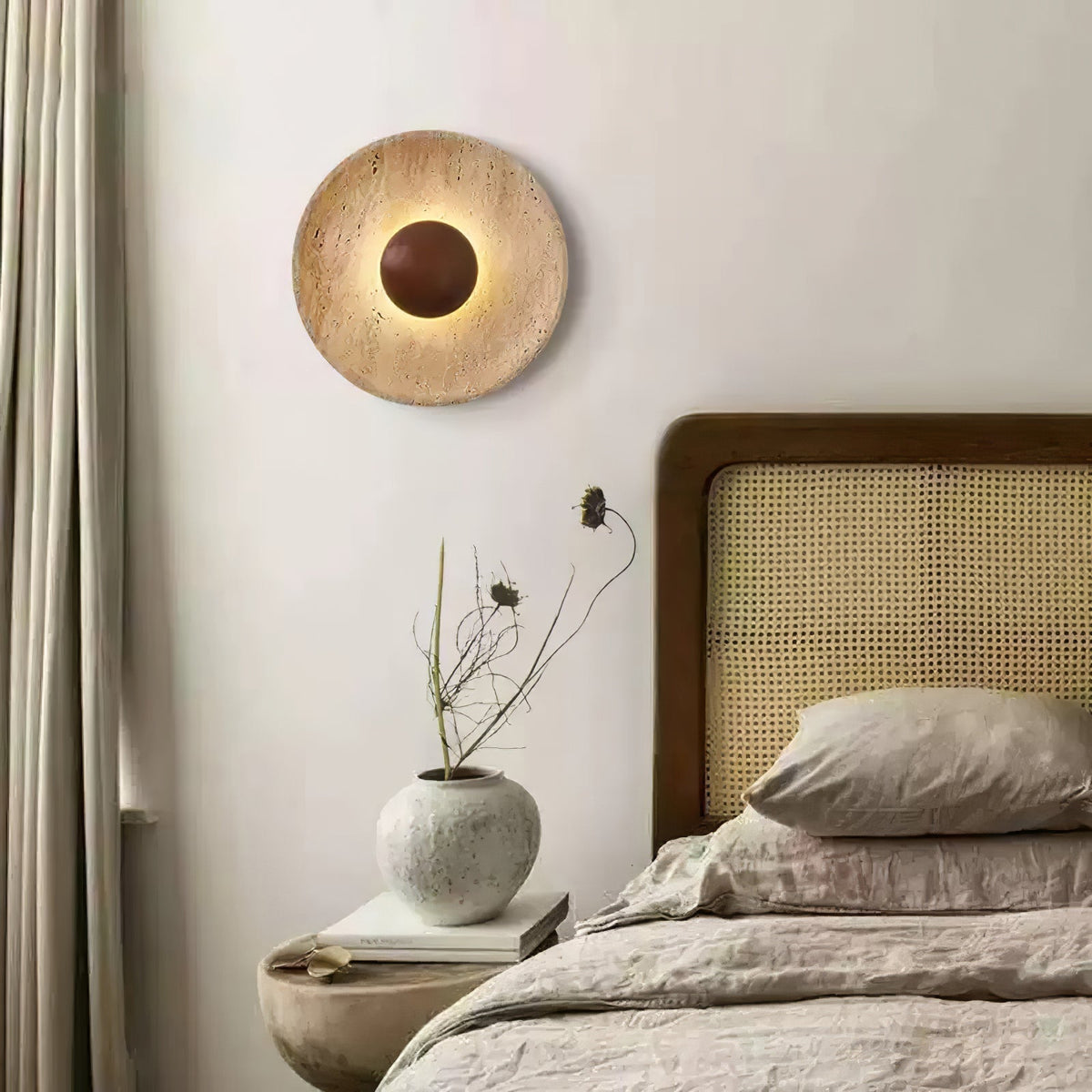 Sunda Travertine Wall Light above a bedside vase and linen bedding in a warm neutral bedroom