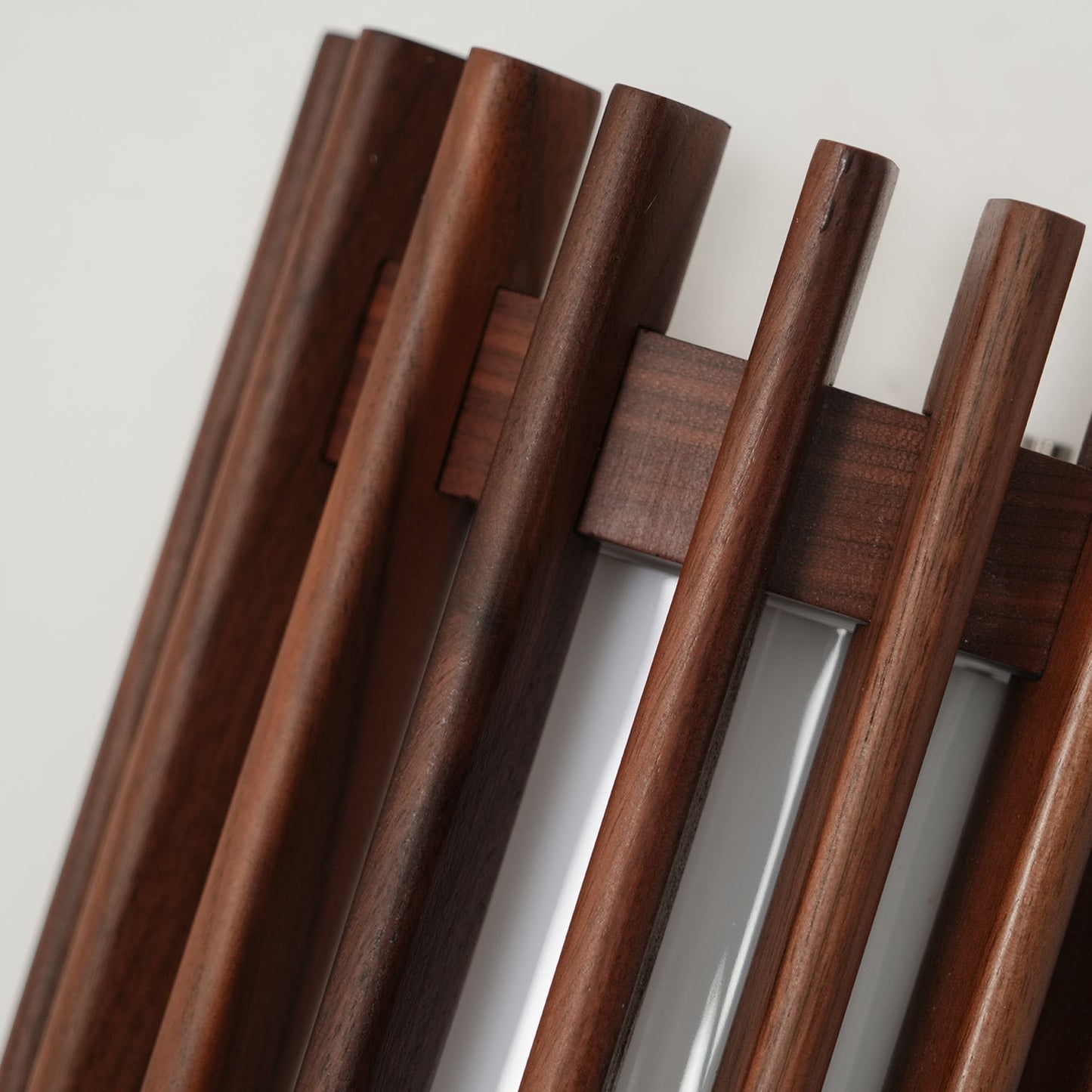 Angled detail of the rounded walnut finish slats and cross rail on the Neyro wall light