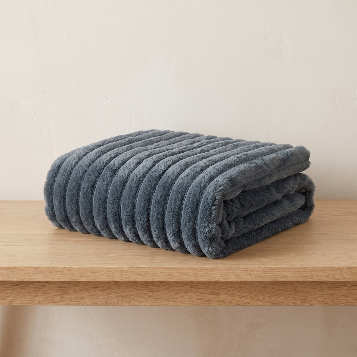 Nordo grey throw blanket neatly folded on a pale oak bench against a warm off-white plaster wall