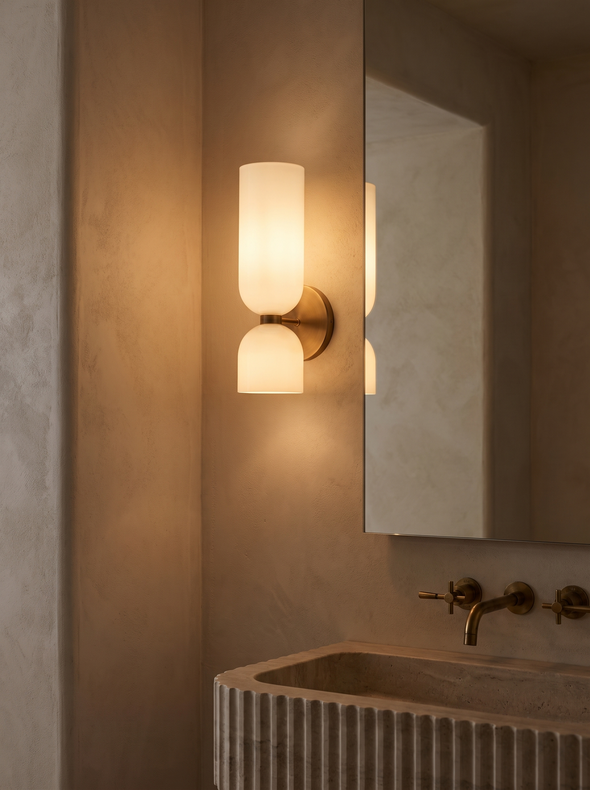 Solia Twin Glass Wall Sconce - bathroom vanity lifestyle, both shades glowing warm 2700K beside frameless mirror above fluted travertine basin