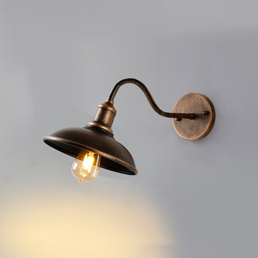 Bolva antique brass barn light mounted on a pale wall, showing the round backplate and swan neck arm