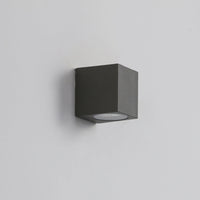 Dovra square outdoor wall light in black mounted on a plain grey wall, compact cube with a recessed lens underneath