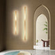 Two Azino Slim LED Wall Lights glowing vertically on a warm beige hallway wall beside arched doorways