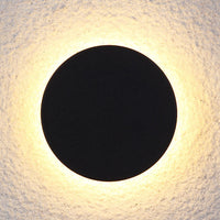Close view of the Klyno black round outdoor wall light casting a warm halo on a textured wall