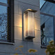 Rekta rectangular wall light glowing on a stone facade between windows at dusk