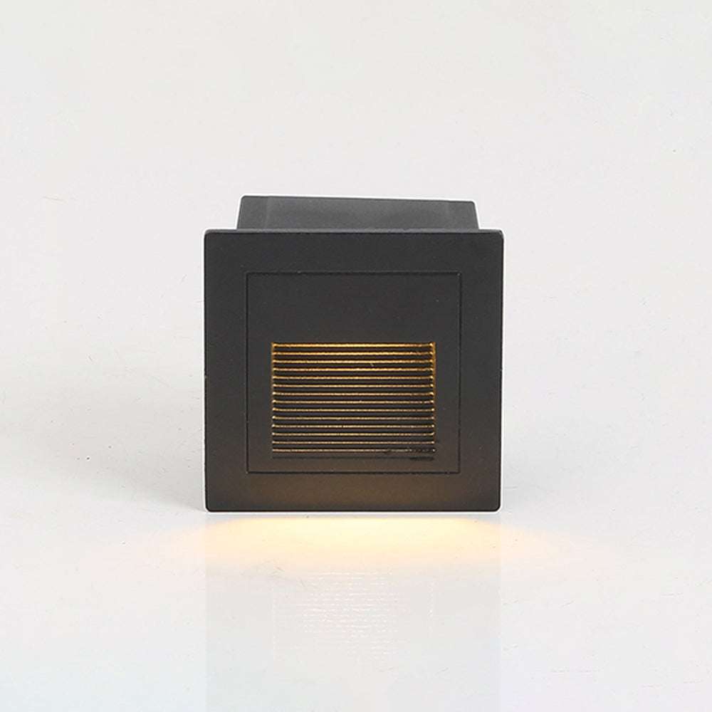 Black Steva square step light shown at an angle with its recessed back box, casting warm light downward