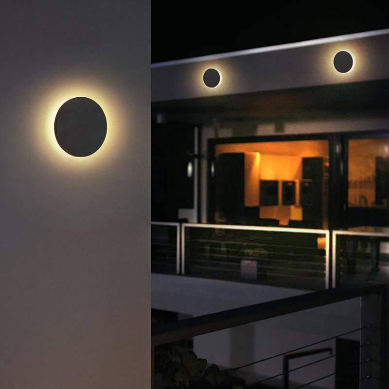 Klyno black round outdoor wall light lighting a wall beside a modern house at night