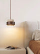 Trava travertine and wood pendant light lit above a bedside table against a plain wall