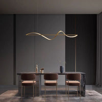 Kavro gold wave pendant lit above a dark dining table with upholstered chairs