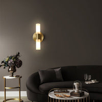 Brenlo twin cylinder wall light lit on a dark wall above a curved sofa