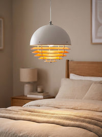 Suno sunset pendant light lit above a bed casting a warm orange glow