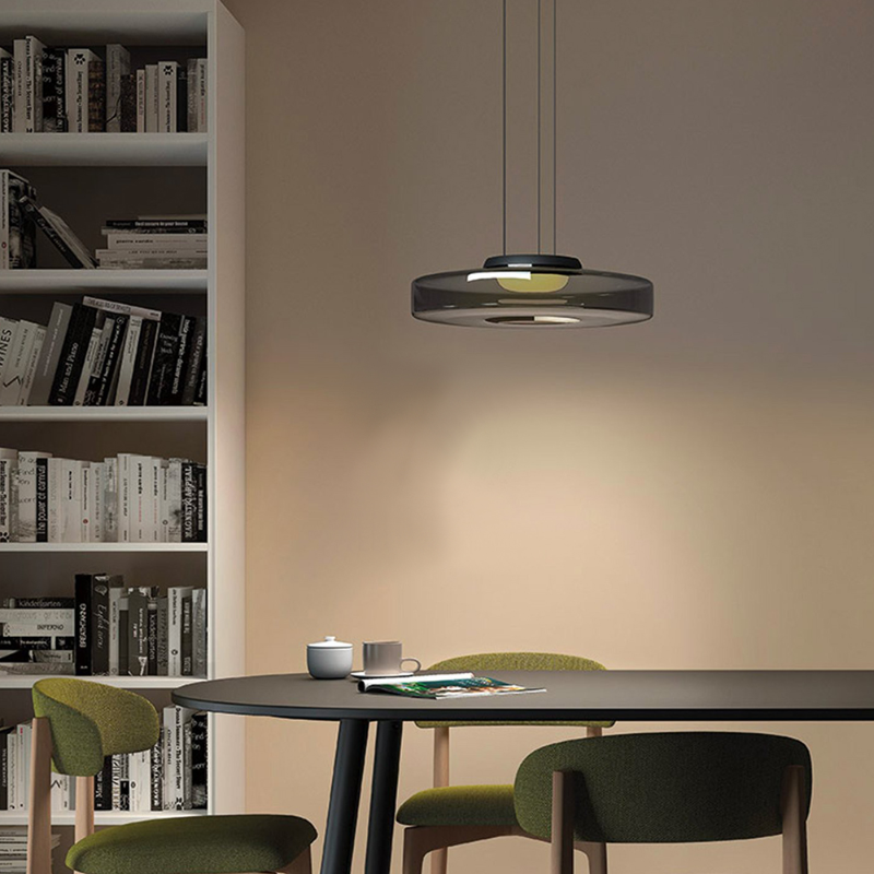 Jovo smoke grey glass pendant hanging above a dining table beside a bookshelf