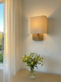 Lino Curved Linen Wall Light lit at dusk, casting a warm glow up and down the wall
