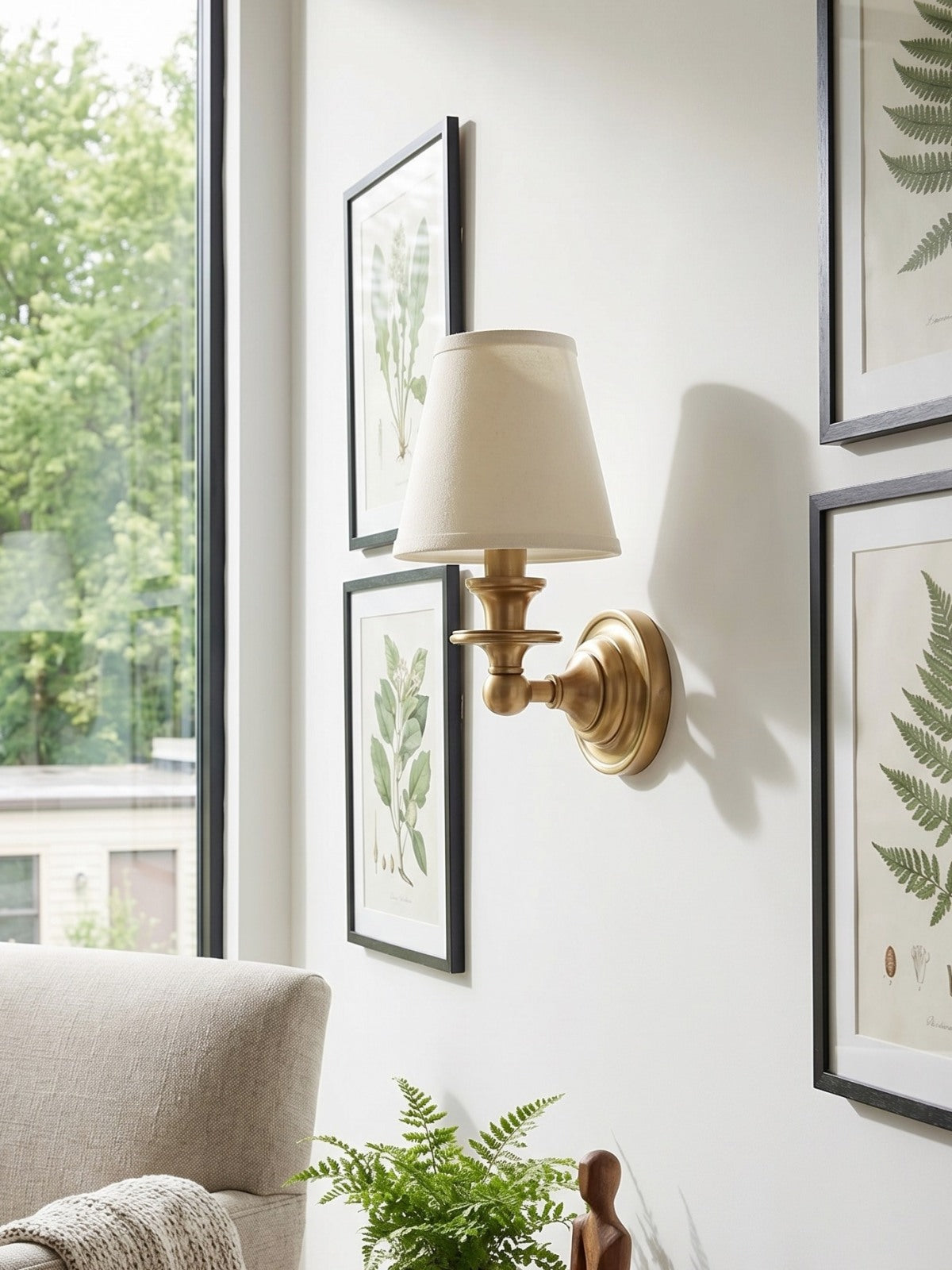 Ruva brass wall light mounted beside framed botanical prints in a living room