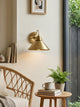 Arvo Bronze Cone Wall Light lit above a reading corner with rattan chair and side table