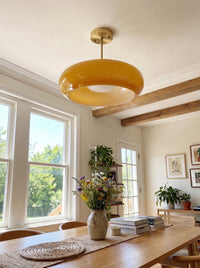 Amber glass disc ceiling light above a wooden dining table in a beamed room