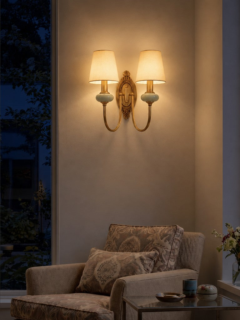 Orla Twin Fabric Shade Wall Light lit in the evening, casting a warm glow over a reading chair
