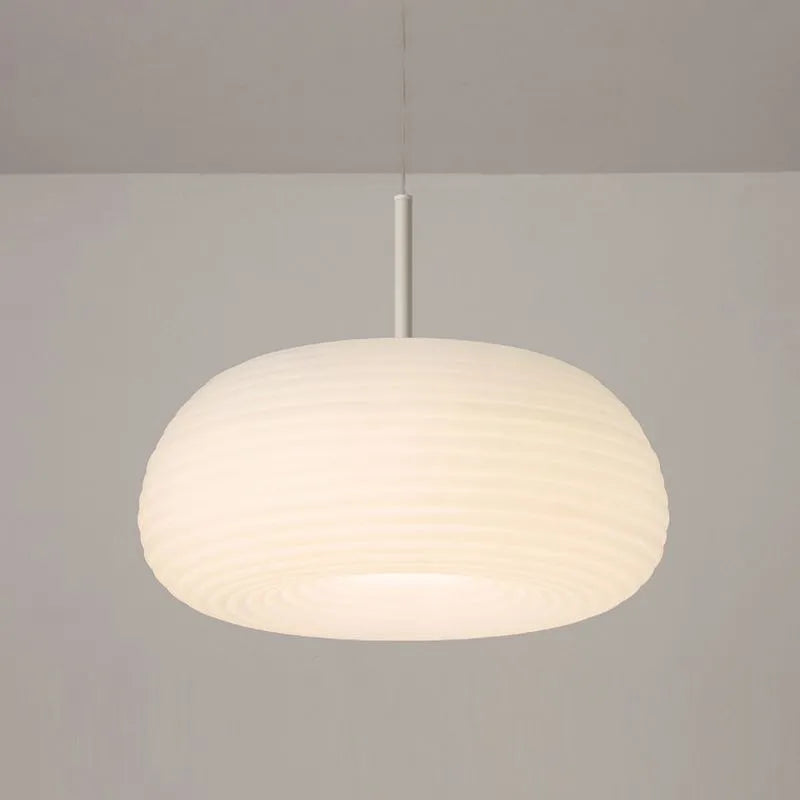 Ombia pendant lit in a neutral white setting, showing the ribbed shade glowing evenly