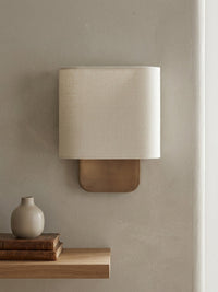 Lino Curved Linen Wall Light in natural linen above a floating oak shelf with books and a vase