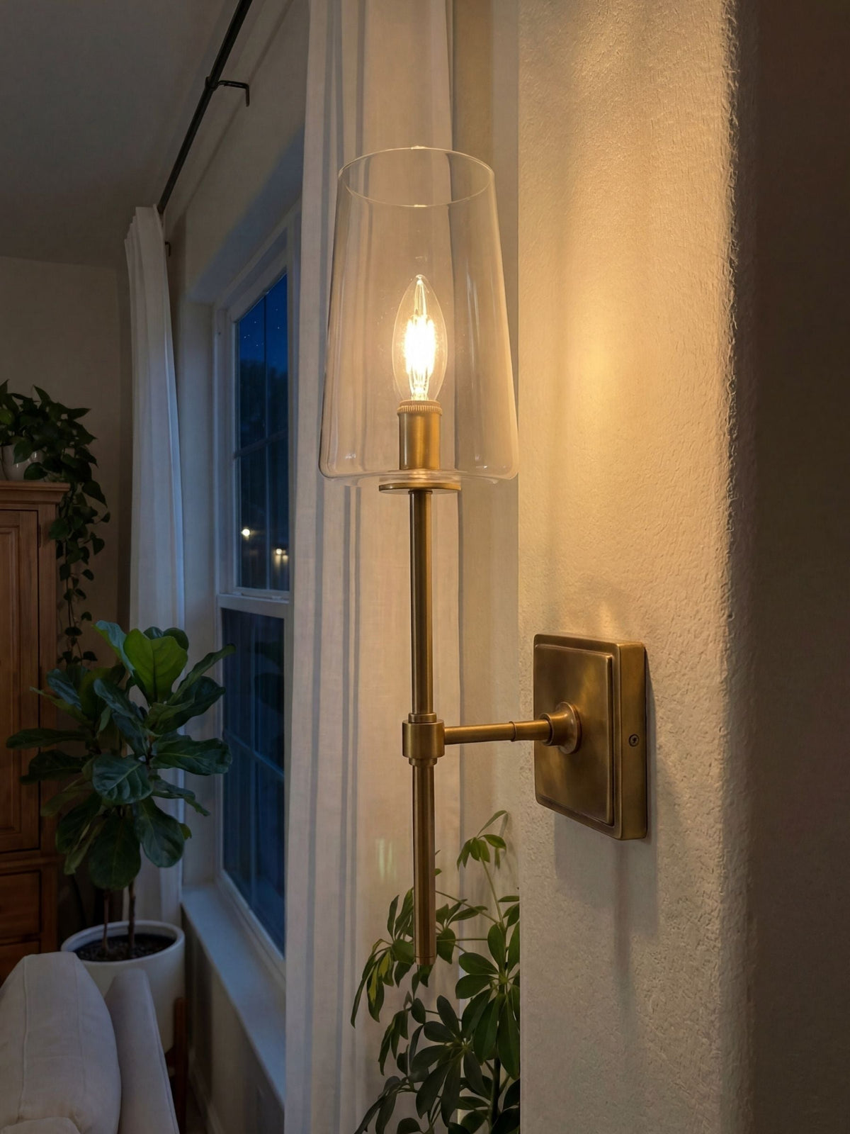 Torin Clear Glass Wall Sconce lit at dusk, warm candle glow against a textured wall