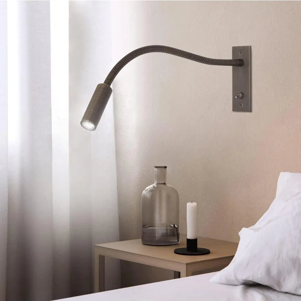 Vexo bronze reading wall light with the gooseneck arm angled over a bedside table