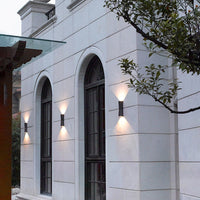 Row of black Kestro Torch wall lights on a pale stone house facade casting warm up and down beams at dusk