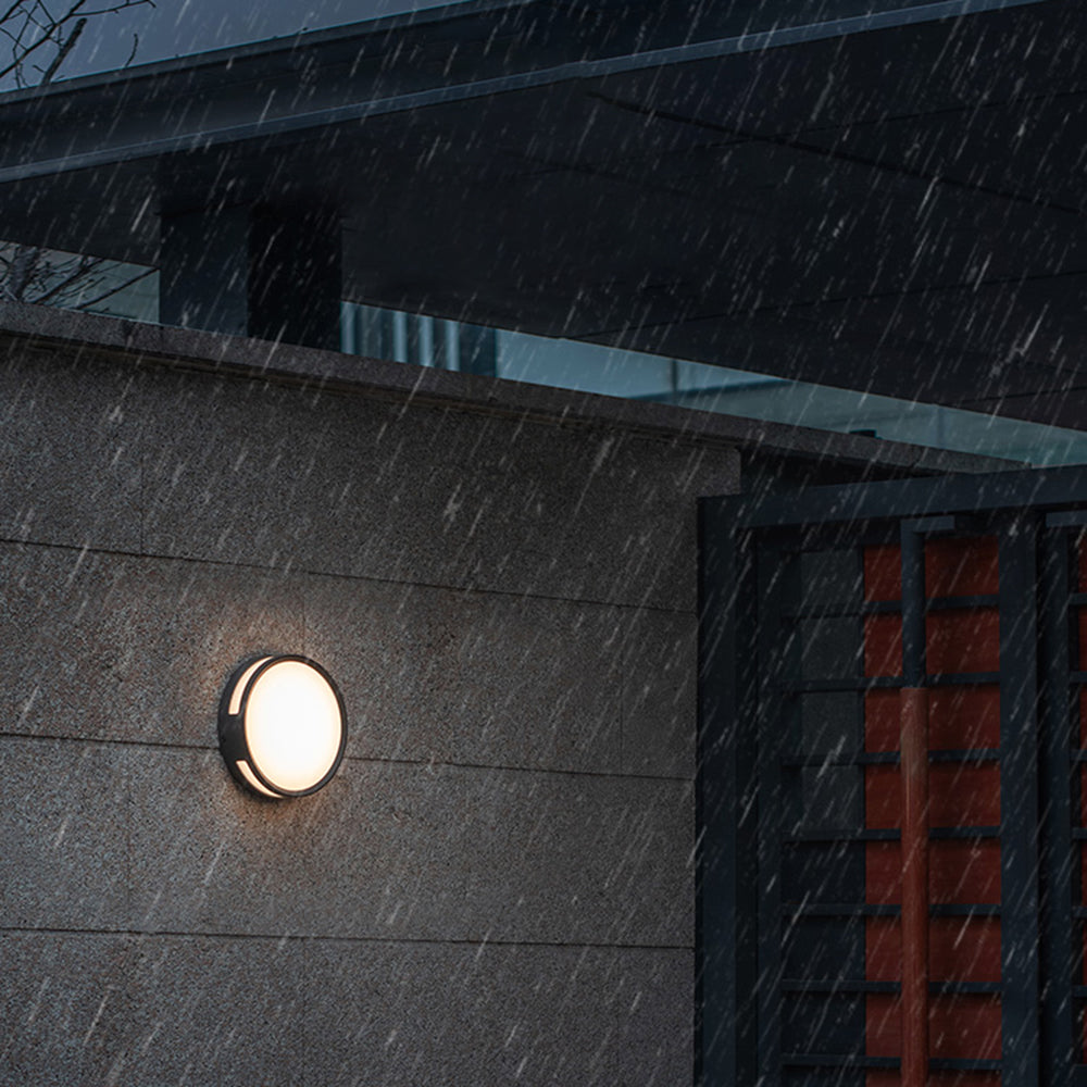 Vardo IP65 outdoor wall light lit on a stone house wall during heavy rain