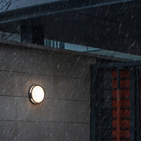 Vardo IP65 outdoor wall light lit on a stone house wall during heavy rain
