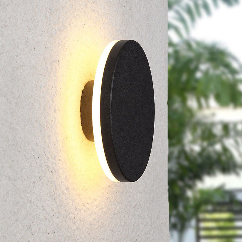 Angled view of the matt black Klyno round outdoor wall light showing its slim profile against a rendered wall