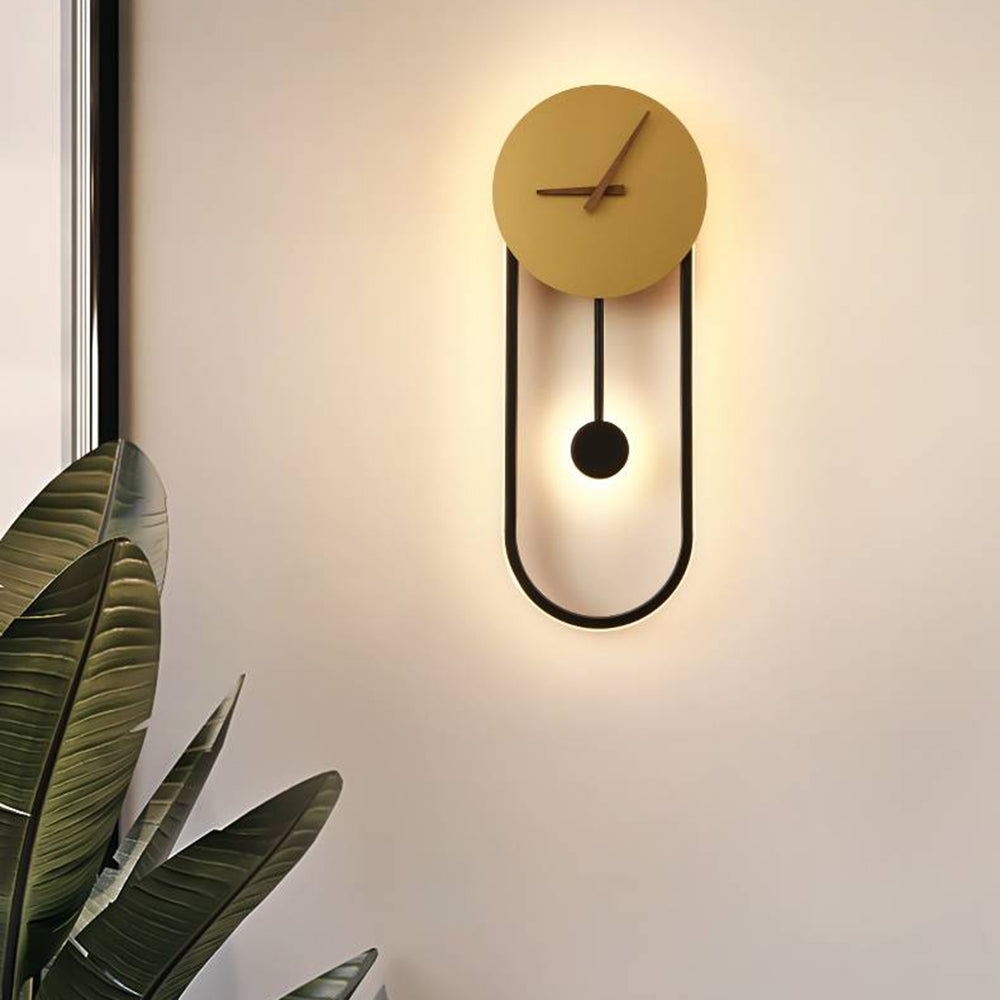 Kalve clock wall light glowing warm on a pale wall beside a large leafed plant