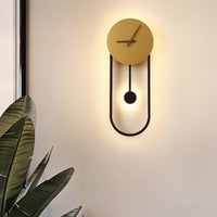Kalve clock wall light glowing warm on a pale wall beside a large leafed plant