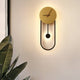 Kalve clock wall light glowing warm on a pale wall beside a large leafed plant