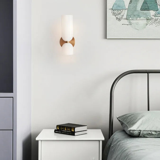 Solia Twin Glass Wall Sconce beside a bed with a white bedside table and books