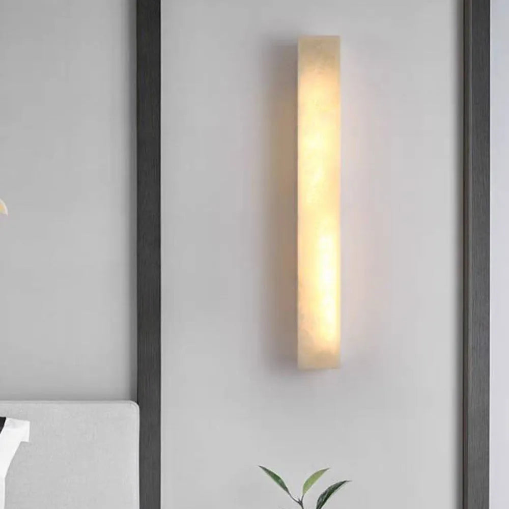 Ayro rectangular wall light glowing warm against a plain wall, showing the veined stone effect in the shade
