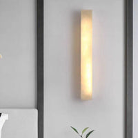 Ayro rectangular wall light glowing warm against a plain wall, showing the veined stone effect in the shade