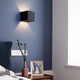 Nexo black wall light casting up and down light on a blue bedroom wall