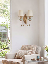 Orla Twin Fabric Shade Wall Light with two white shades and brass swoop arms above an armchair in a bright living room