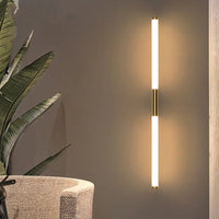 Morva wall light fitted vertically beside a chair, showing the gold bracket at the centre of the lit tube