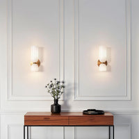 A pair of Solia Twin Glass Wall Sconces lit on a panelled wall above a walnut console table
