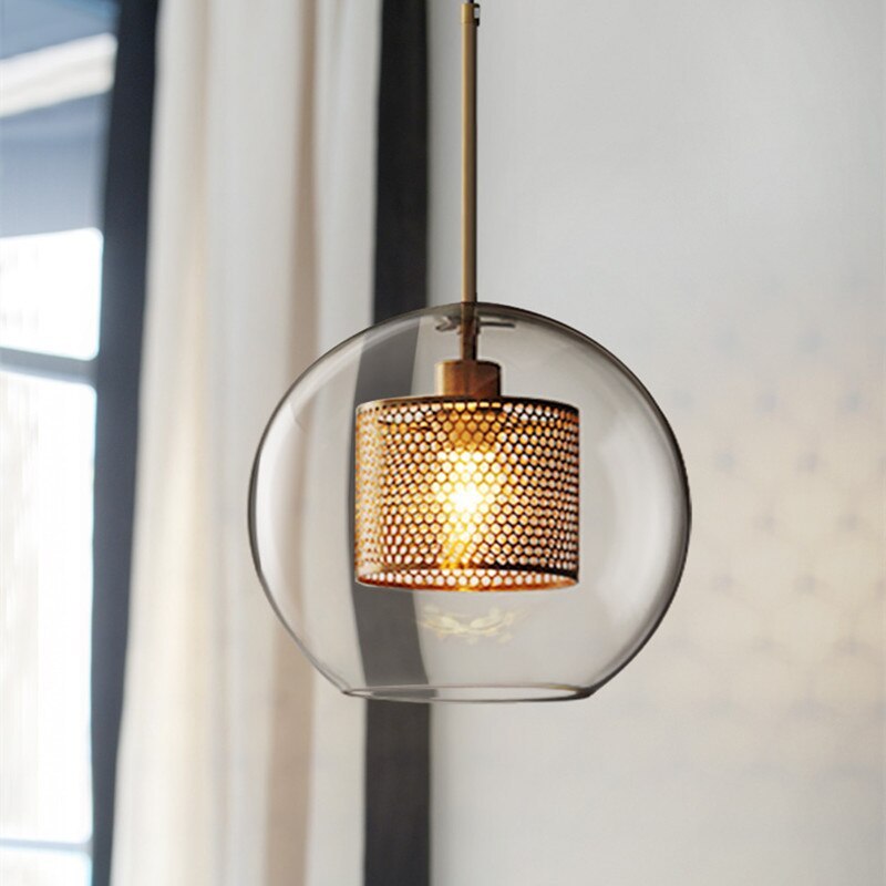 Hesso pendant light lit, showing the perforated brass mesh cylinder inside the glass globe