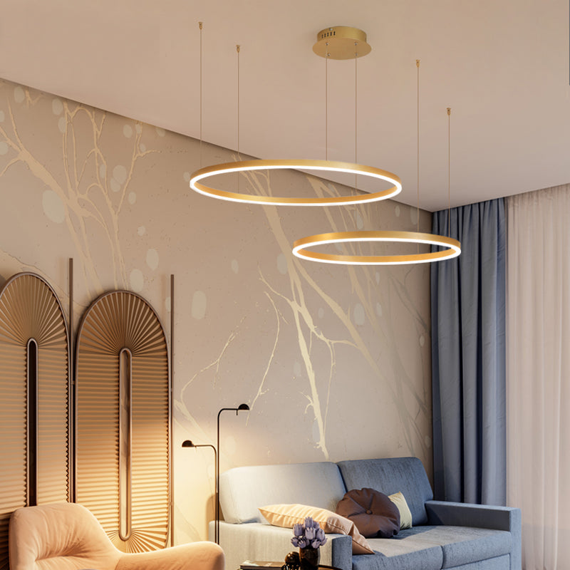 Remo Twin-Ring Pendant Light lit above a living room, gold rings glowing against a pale marbled wall