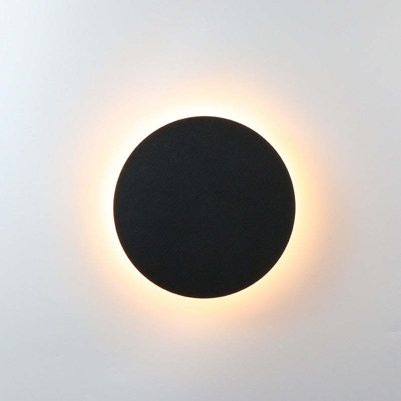 Klyno round outdoor wall light in matt black on a plain pale wall with a warm halo of light