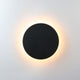 Klyno round outdoor wall light in matt black on a plain pale wall with a warm halo of light