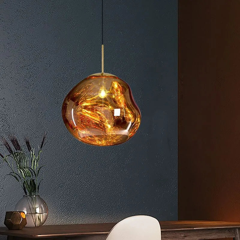 Milto gold pendant hanging against a deep blue wall above a console table, glowing amber through the rippled shade
