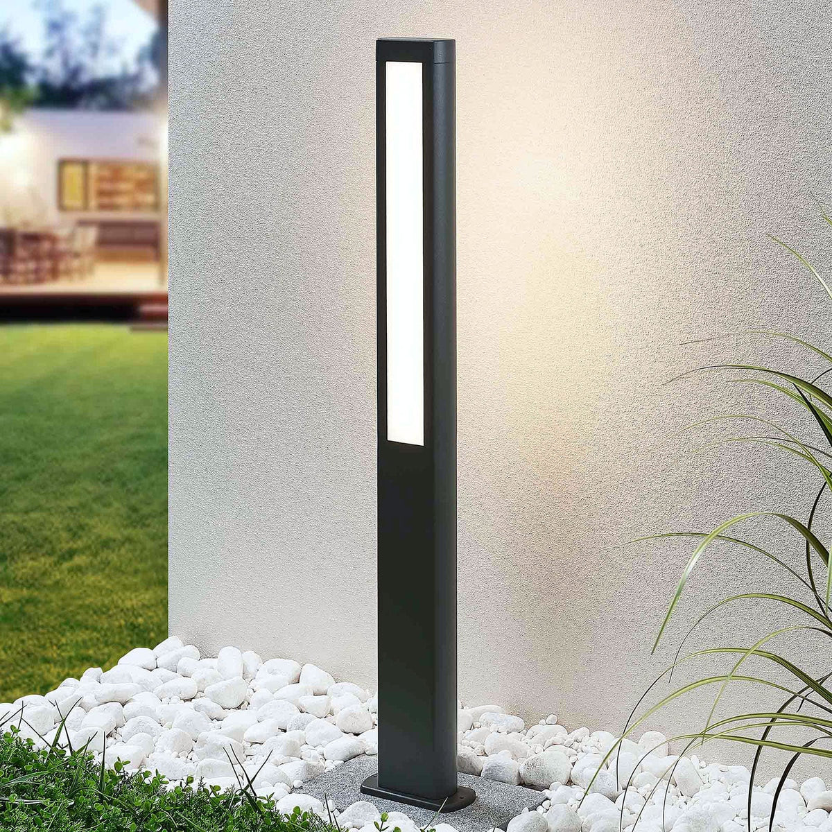 Mairo path light lit against a rendered garden wall beside white pebbles and grass