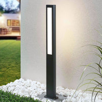 Mairo path light lit against a rendered garden wall beside white pebbles and grass
